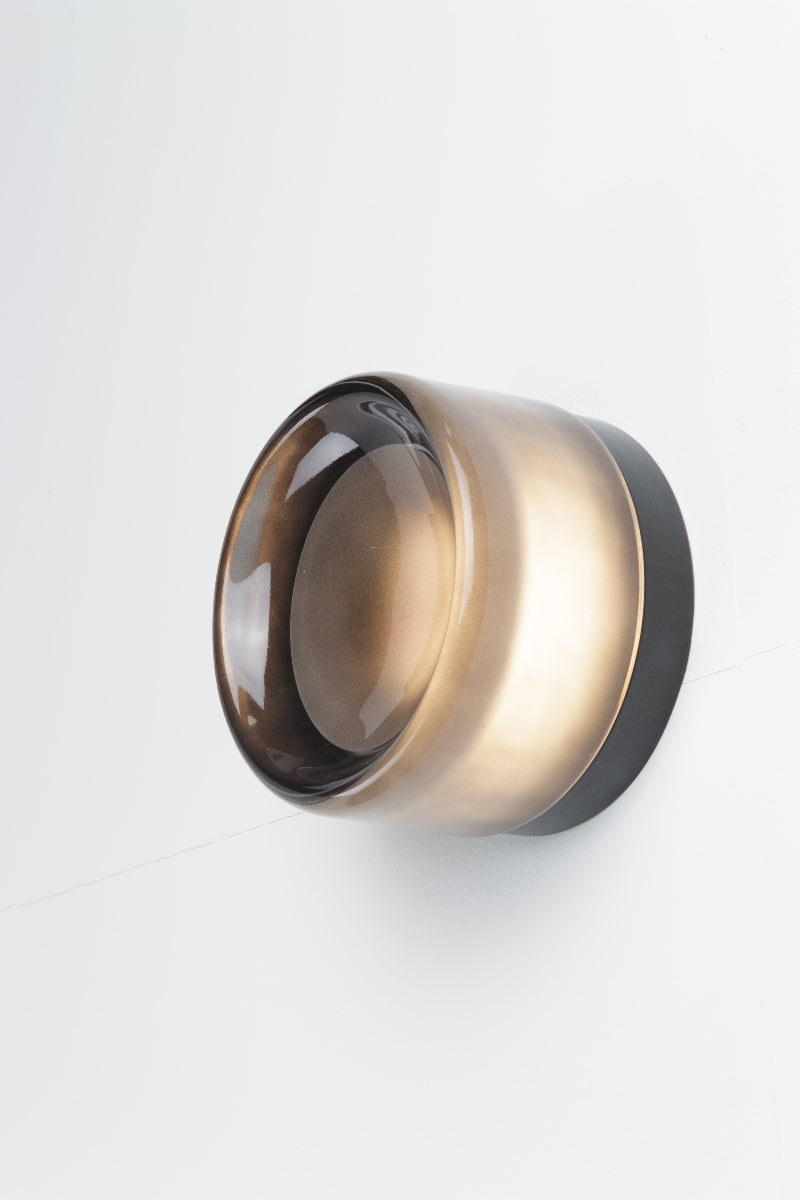 Grey eye catching wall light is comprised of a glass exterior over a built-in light source with dome diffuser.