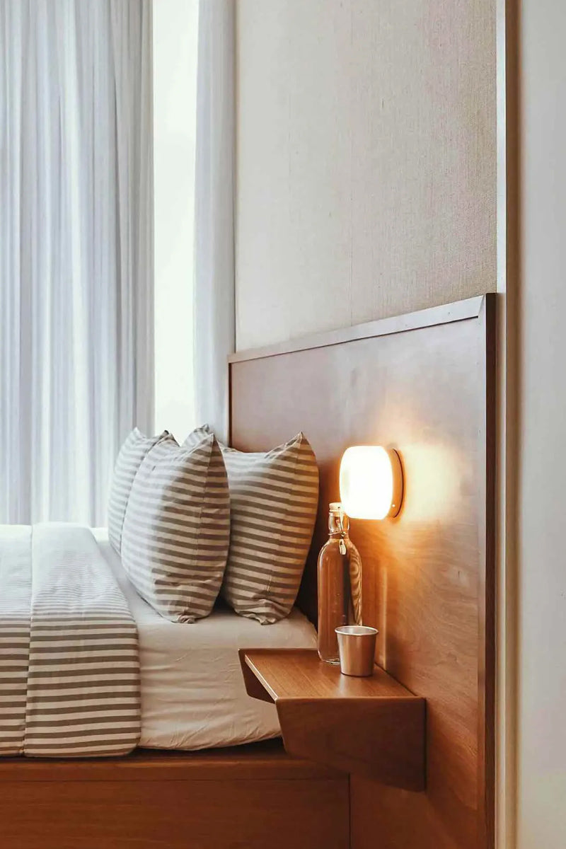 Bedroom with striped bedding, wooden nightstand and white wall sconce as a bedside light