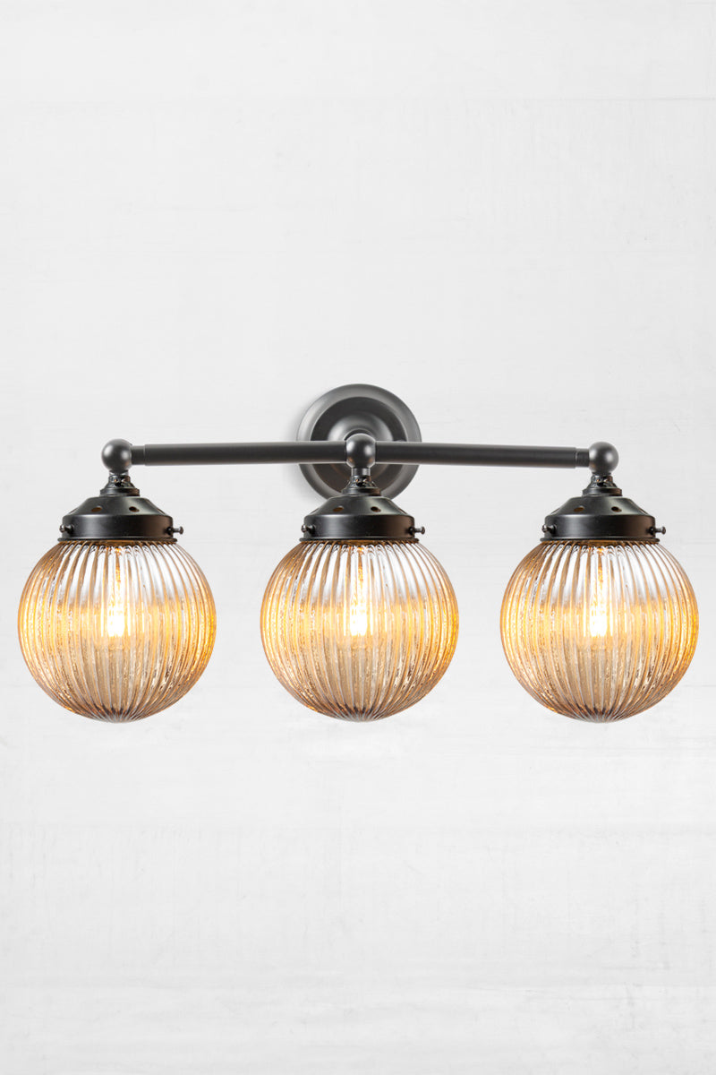 Black three lampholder wall sconce paired with three dark amber reeded glass ball shades. 