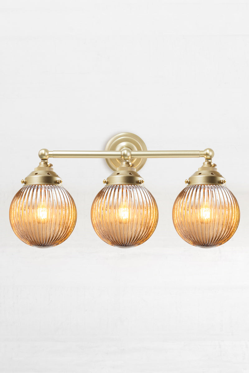 Gold/Brass three lampholder wall sconce paired with three dark amber reeded glass ball shades. 