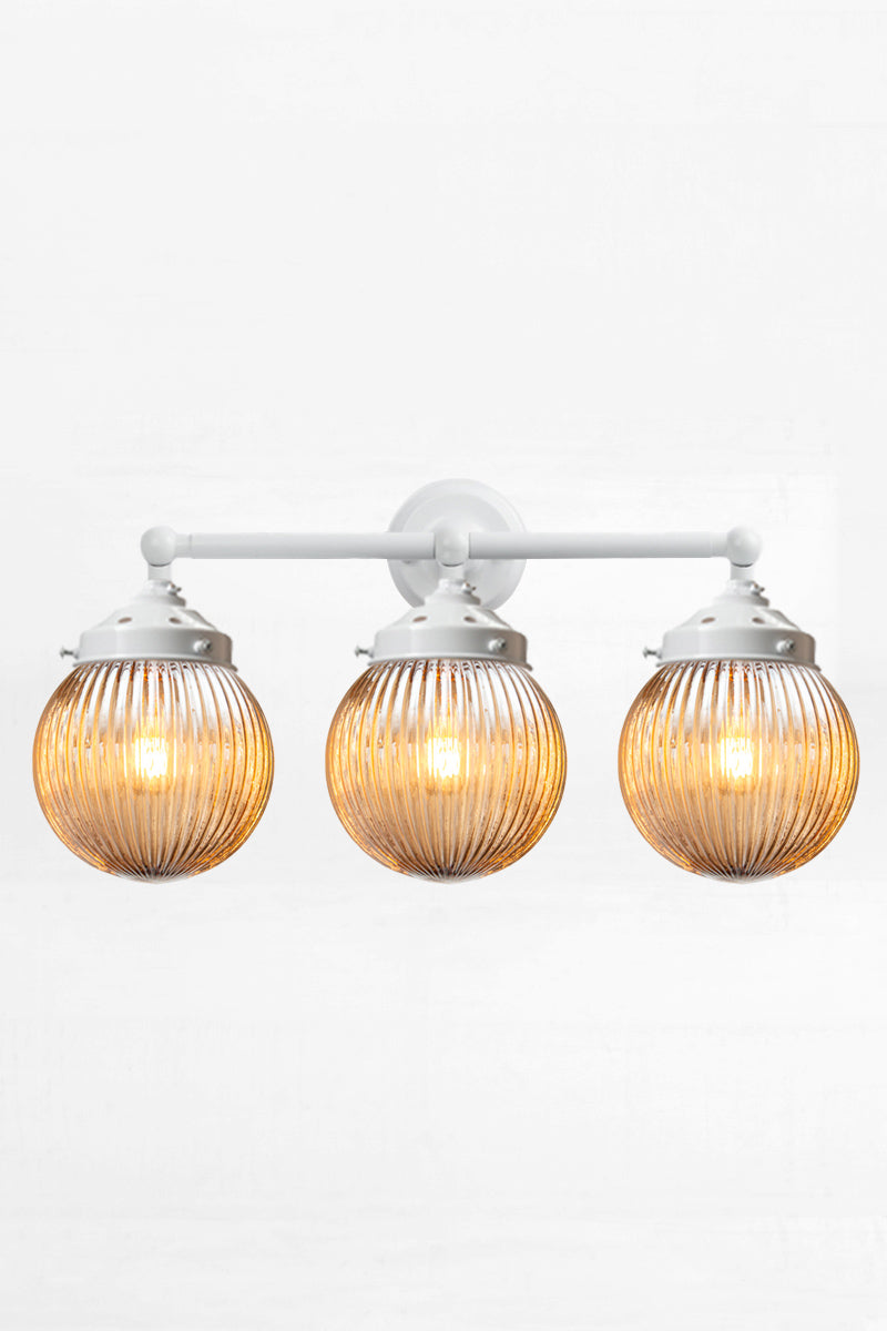 White three lampholder wall sconce paired with three dark amber reeded glass ball shades. 