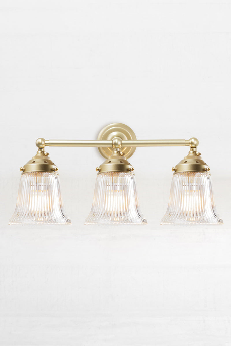 Front facing triple gold/brass wall sonce with clear reeded glass shades. 