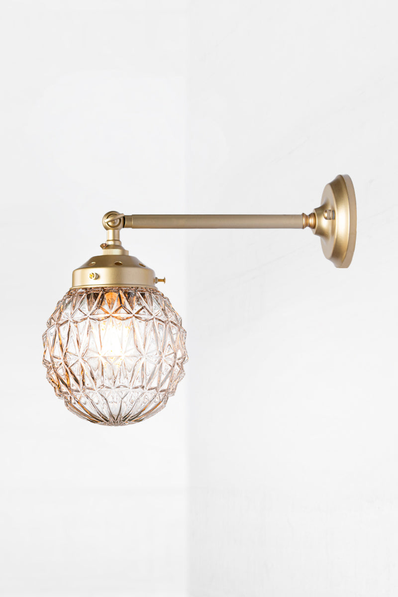 Long straight arm wall sconce with tiltable lampholder in black paired with a clear glass orb shade with vintage detailing. 