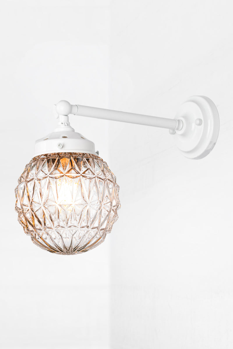 Long white, straight arm wall sconce with tiltable lampholder paired with a clear glass orb shade with vintage detailing. 