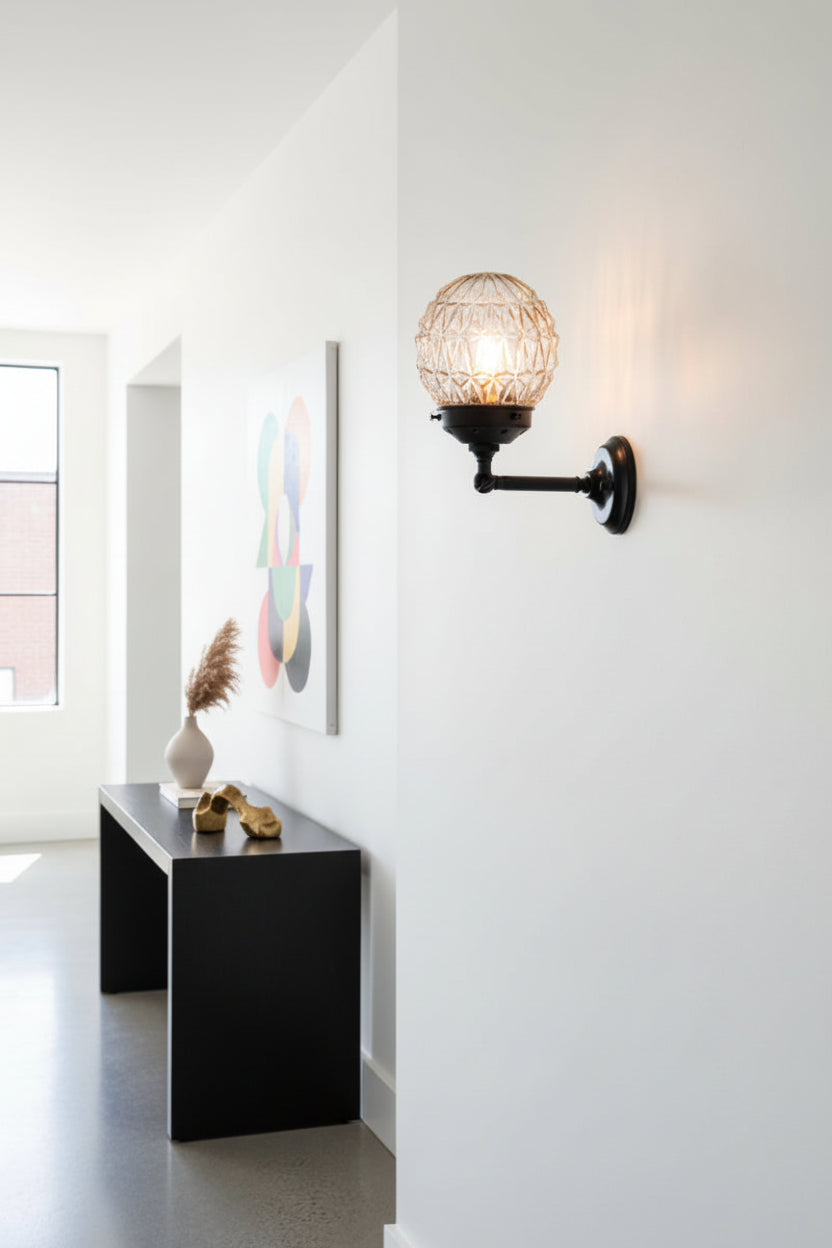 Clear glass orb shade with vintage detailing paired with a short black steel wall sconce in a contemporary hallway. 