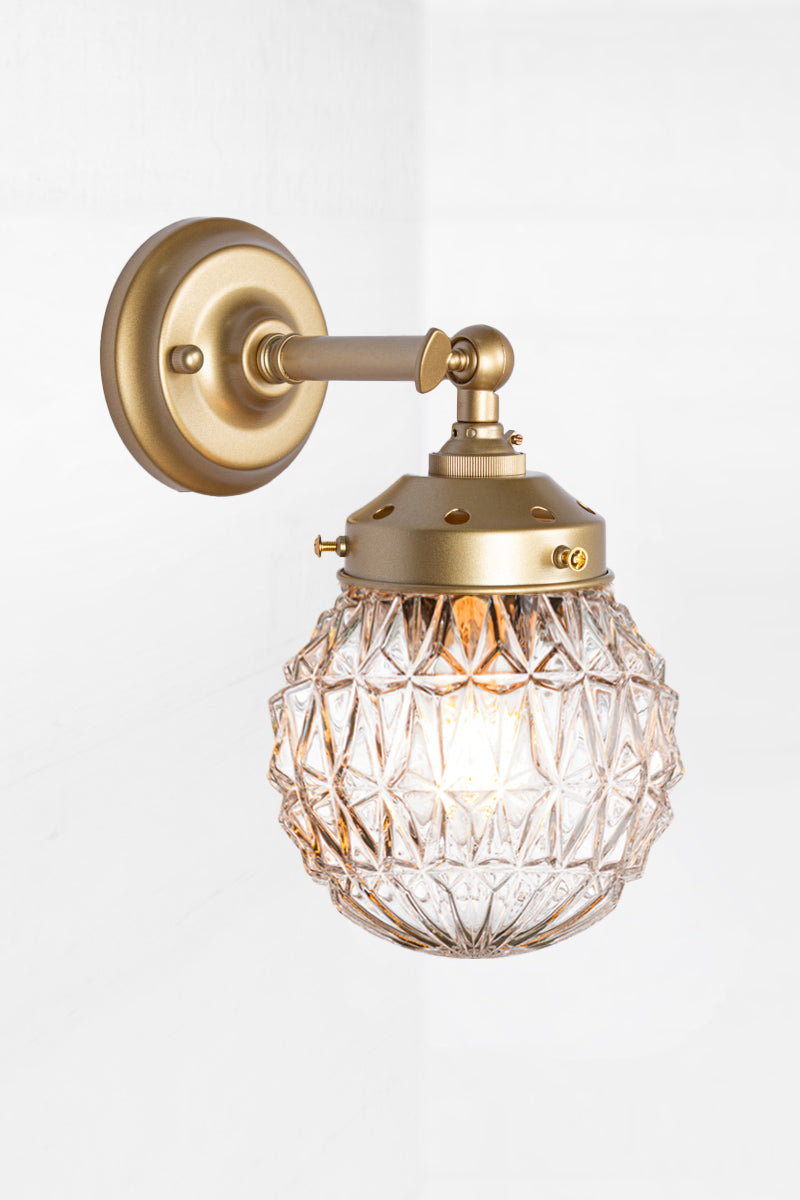 Short straight arm wall sconce with tiltable lampholder in gold/brass paired with a clear glass shade cut glass detailing. 