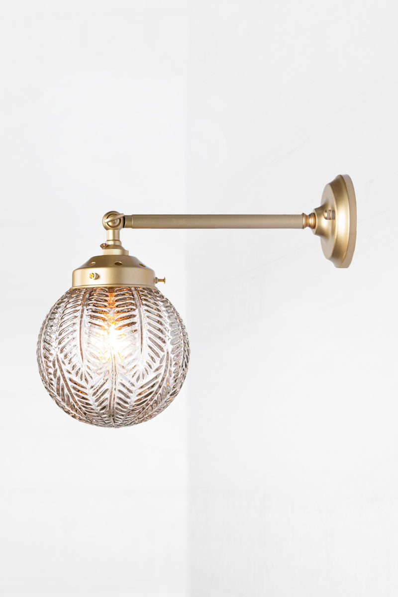 Long straight arm wall sconce with tiltable lampholder in black paired with a clear glass orb shade with intricate detailing. 