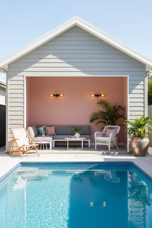A modern outdoor patio area with a swimming pool and cabana featuring a pink wall and 2 wall lights