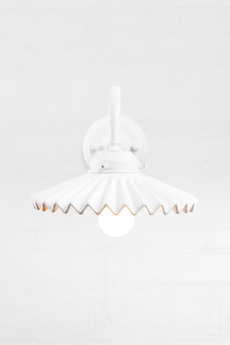 Front view of the white gooseneck wall arm with an integrated 2 and 1/4 cup, paired with a white ceramic shade, showcasing the pleated detail.