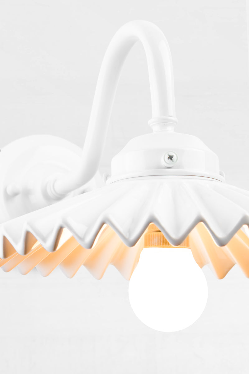 Close up of the white gooseneck wall arm with an integrated 2 and 1/4 cup, paired with a white ceramic shade, with pleated detailing. 