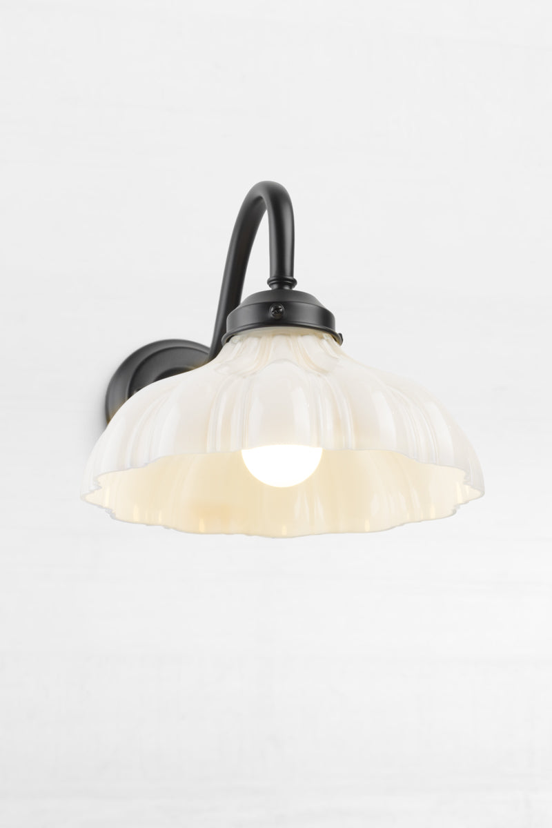 Front view of the black gooseneck wall sconce with integrated gallery, paired with an opal glass shade with vintage detailing.