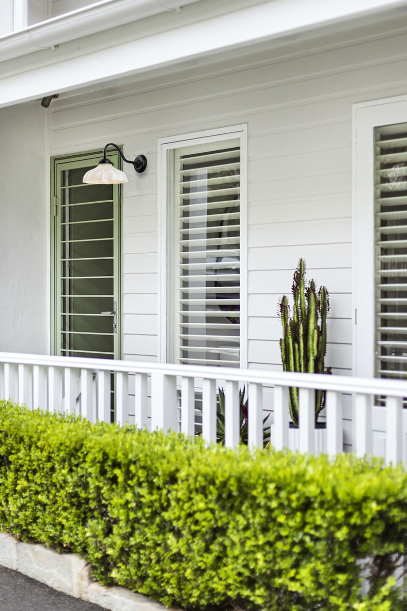 Black gooseneck wall light with opal finished shade on a white weather baord house. 