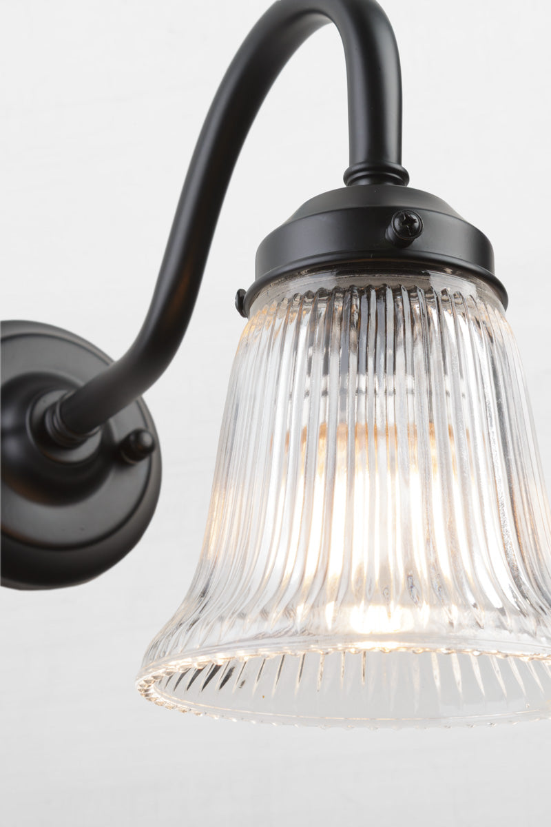Close up of the black gooseneck wall sconce with integrated gallery, showcasing the ribbed detailing of the clear glass shade. 