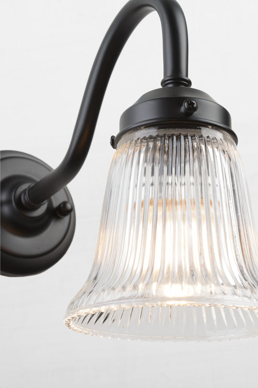 Close up of the black gooseneck wall sconce with integrated gallery, showcasing the ribbed detailing of the clear glass shade. 