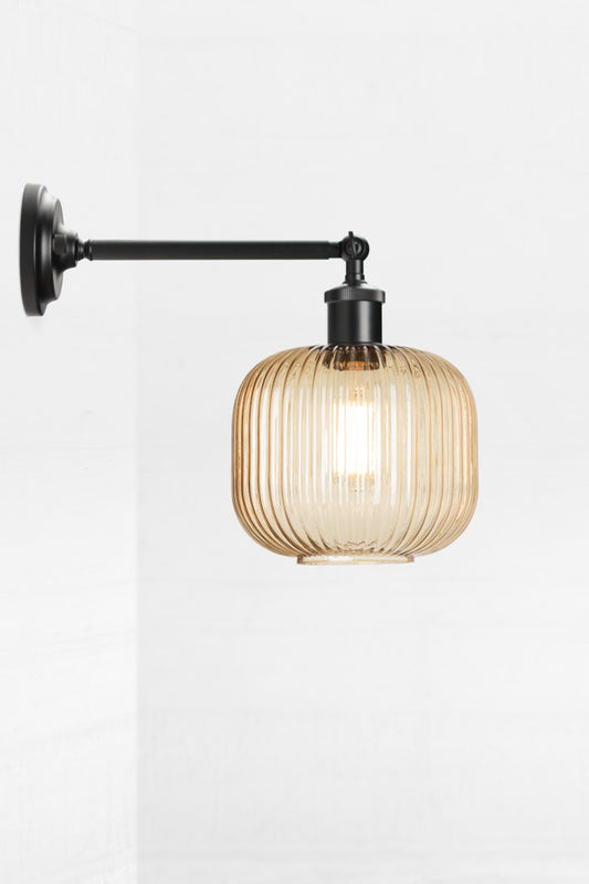 Black swivel wall sconce with long arm and a reeded glass shade in amber. 