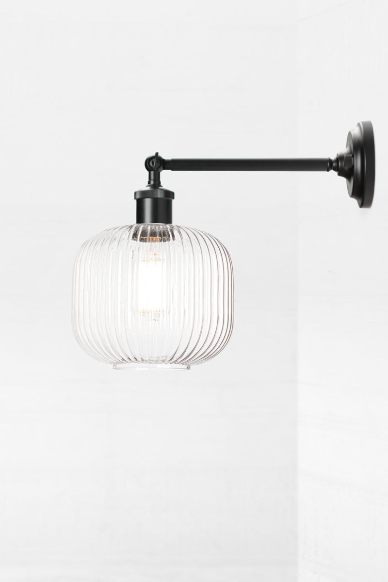 Black swivel wall sconce with long arm and a reeded glass shade in clear. 