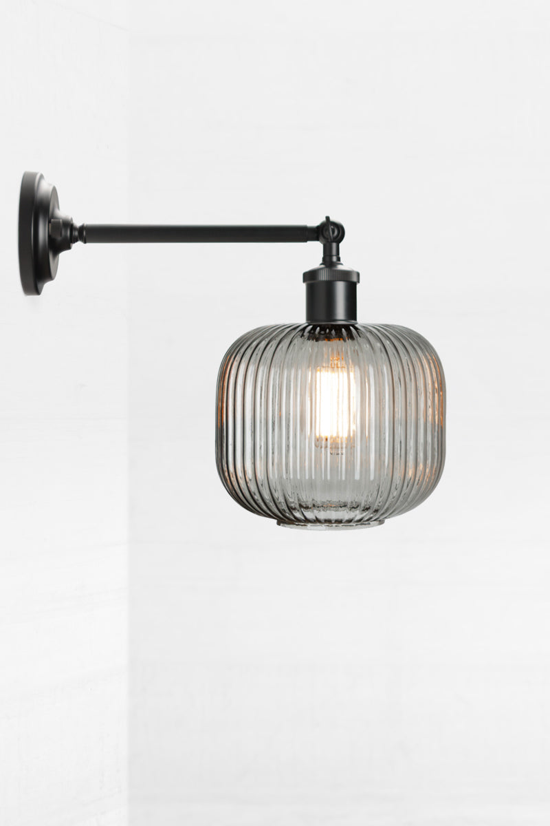 Black swivel wall sconce with long arm and a reeded glass shade in grey. 