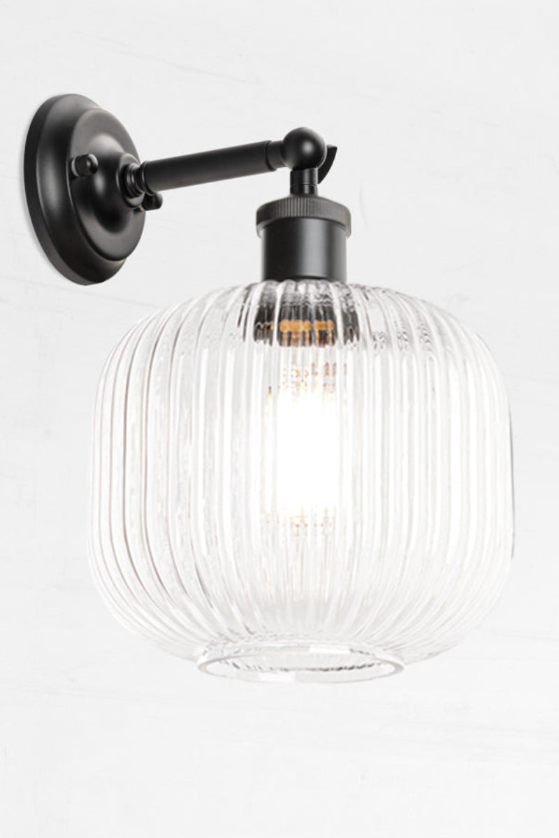 Black swivel wall sconce with short arm and a reeded glass shade in clear. 