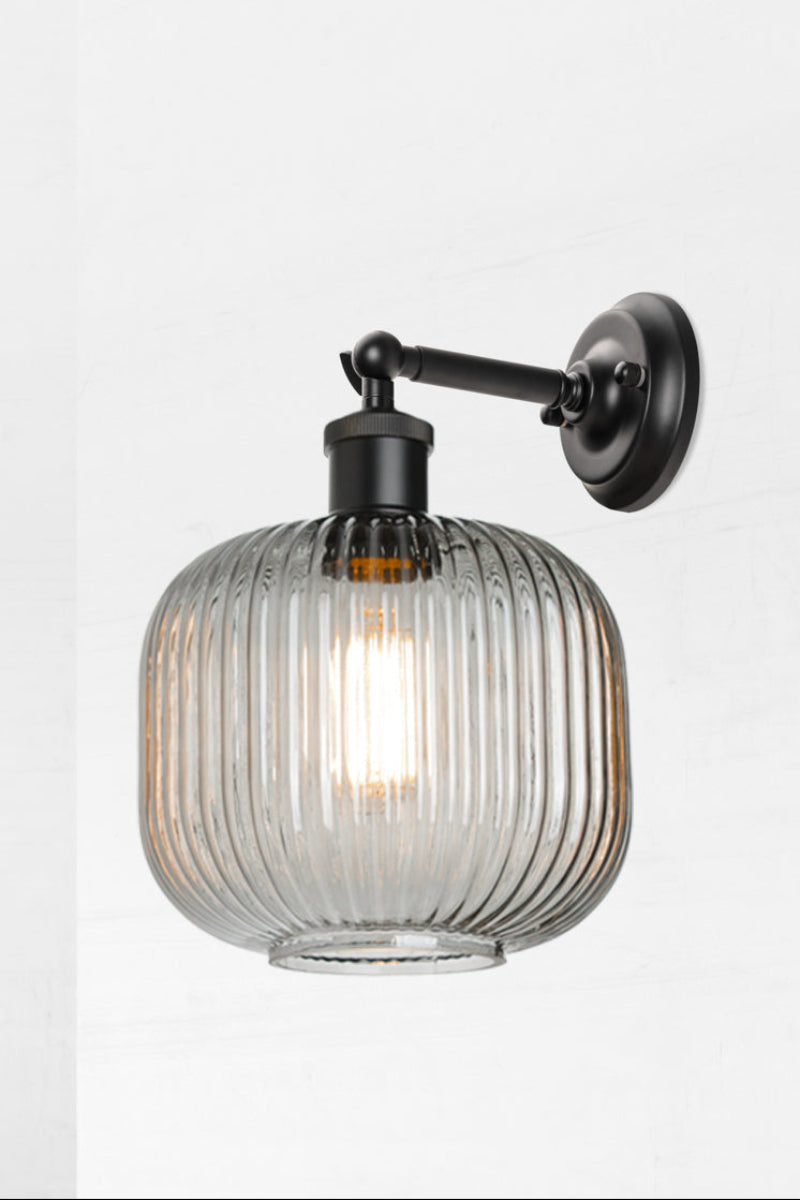 Black swivel wall sconce with short arm and a reeded glass shade in grey. 