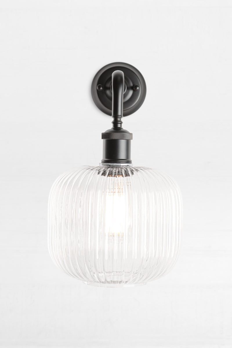 Front view of open clear glass reeded shade paired with a black 90 degree wall sconce. 