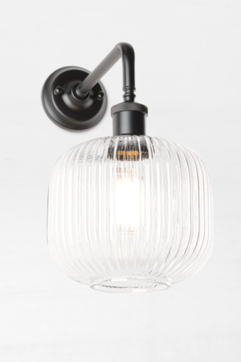 Open clear glass reeded shade paired with a black 90 degree wall sconce. 