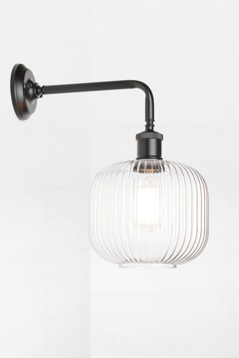 Side view of the open clear glass reeded shade paired with a black 90 degree wall sconce. 
