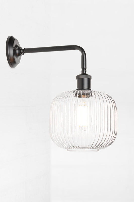 Side view of the open clear glass reeded shade paired with a black 90 degree wall sconce. 