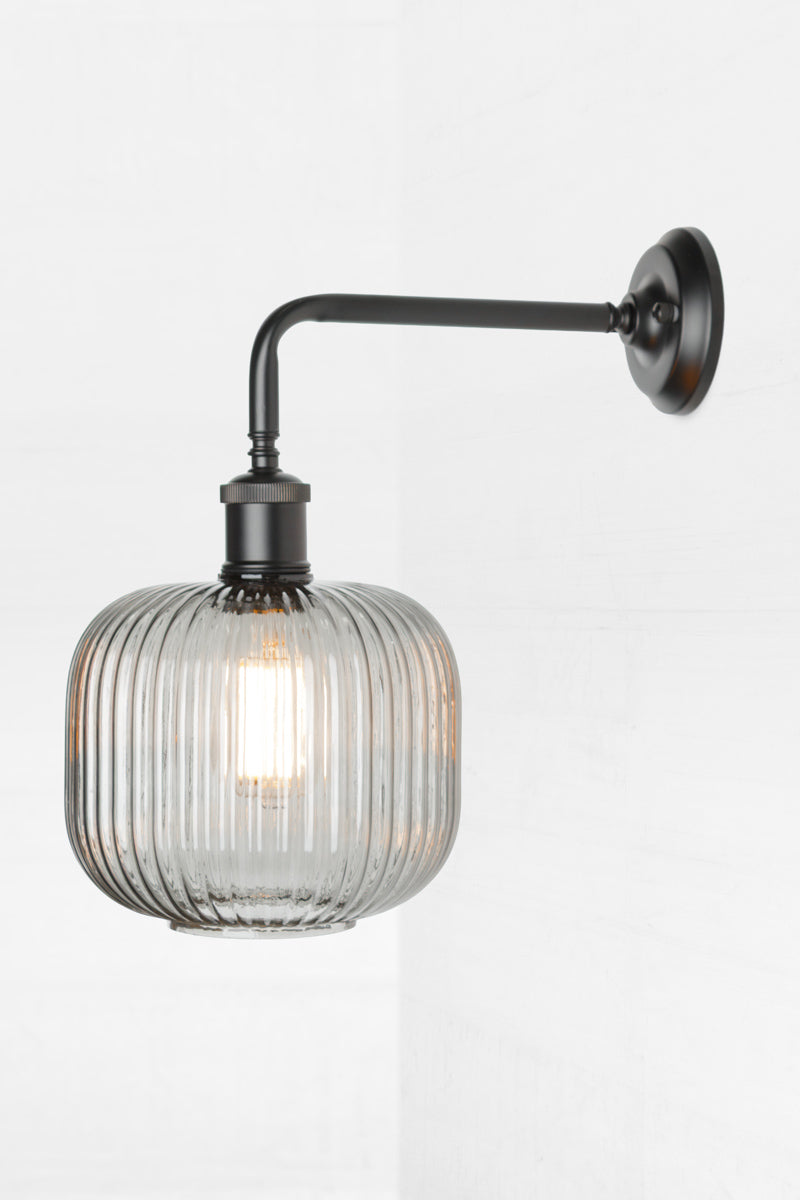 Side view of the open grey glass reeded shade paired with a black 90 degree wall sconce. 