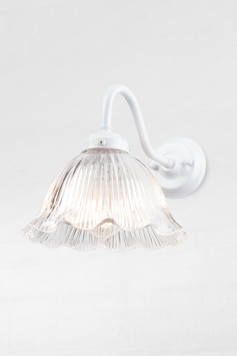White gooseneck outdoor wall light with a clear glass shade that has a ribbed detiling and frill edge. 