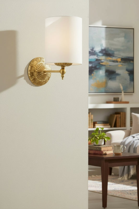 Antique gold finished wall sconce with heritage detailing and a ivory satin shade above a reading nook. 