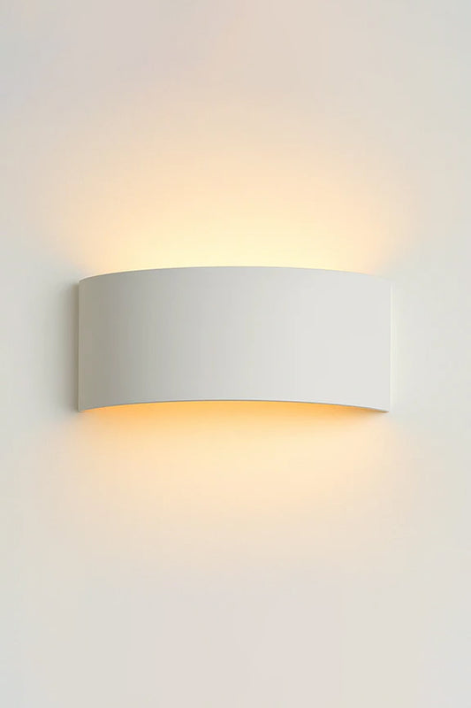 White curved plaster wall light mounted on a white wall, casting a soft warm glow upward and downward.