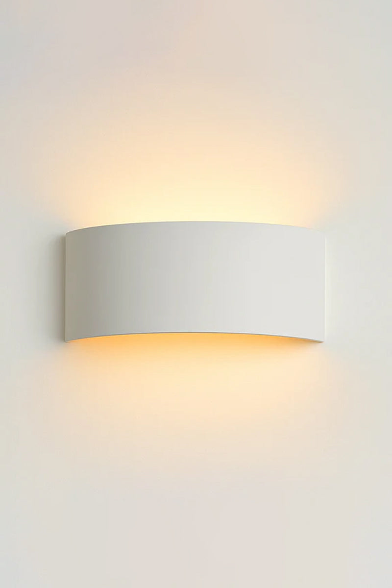 White curved plaster wall light mounted on a white wall, casting a soft warm glow upward and downward.