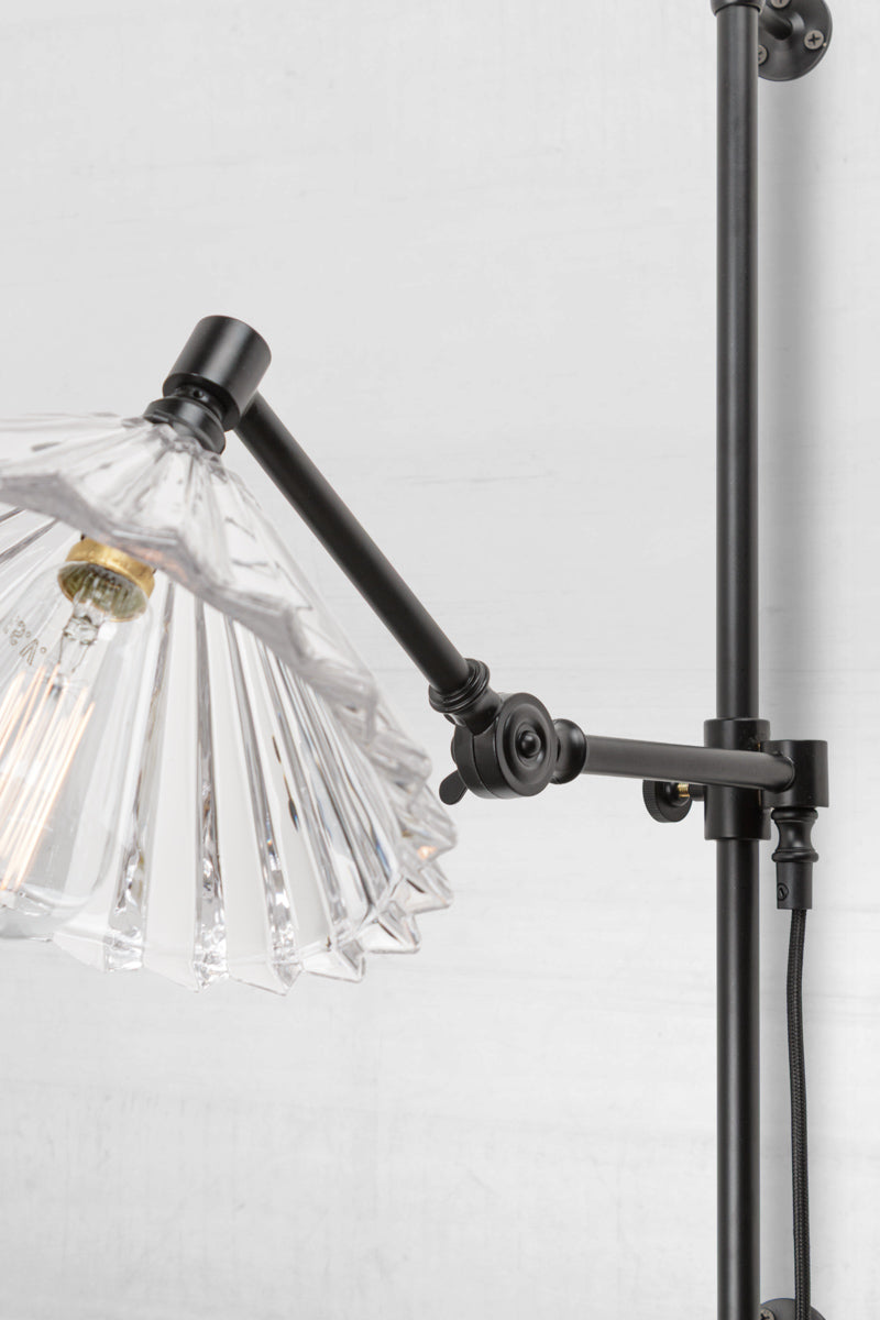 Close up of the black swing wall arm with wall plug and a clear glass pleated shade. 
