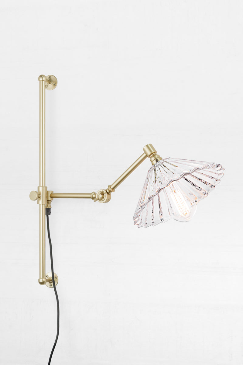 Gold/brass swing wall arm with wall plug and a clear glass pleated shade. 