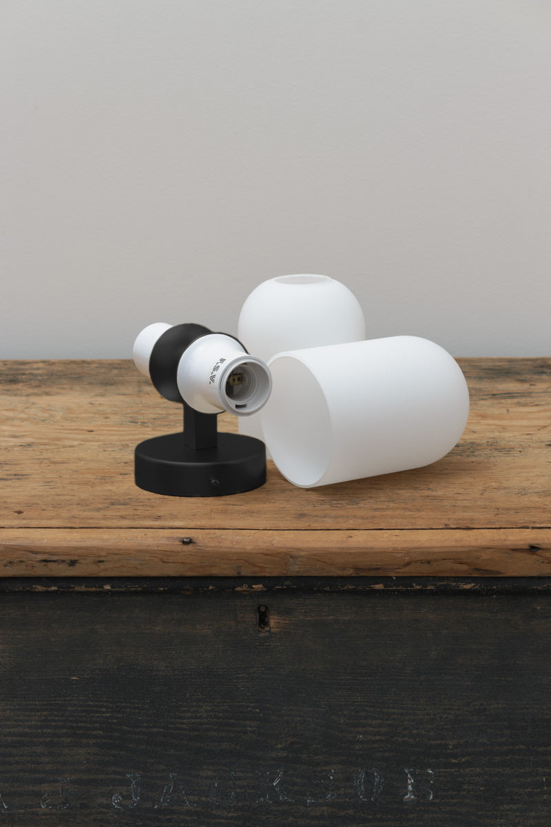 Unintsalled double light wall sconce in black with two opal glass shades placed on a bench. 