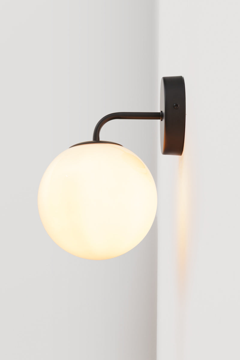 Boise Amber Glass Wall Light installed on a white wall with softly illuminated amber globe shade and black curved arm.