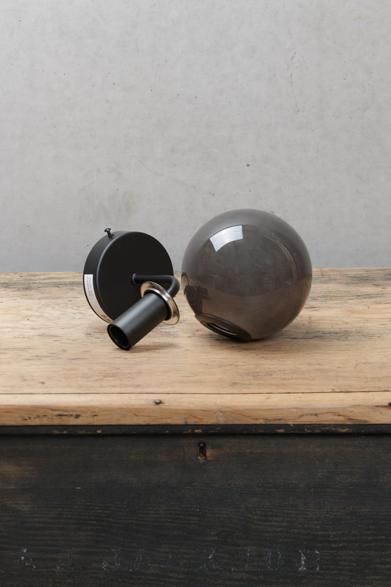 Boise Dark Grey Glass Wall Light with black wall fixture and smoky globe shade displayed on a timber surface.