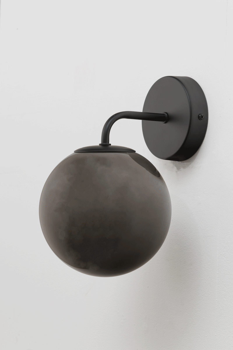 GIF of the Boise Dark Grey Glass Wall Light with black curved arm and smoky dark grey globe shade mounted on a white wall.