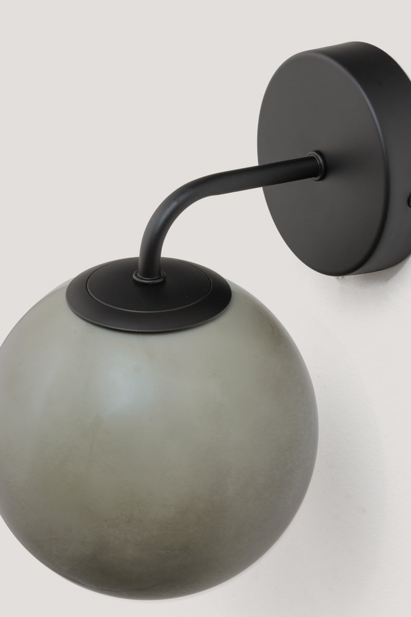 Boise Grey Glass Wall Light with black wall plate and smoked grey globe shade shown mounted on a white wall.