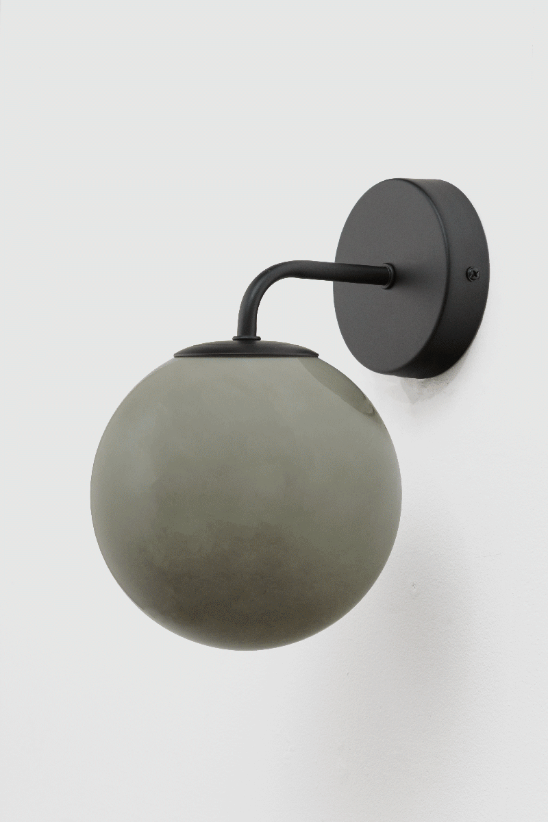 Boise light grey Glass Wall Light with illuminated amber globe shade and black curved arm viewed from an alternate angle.