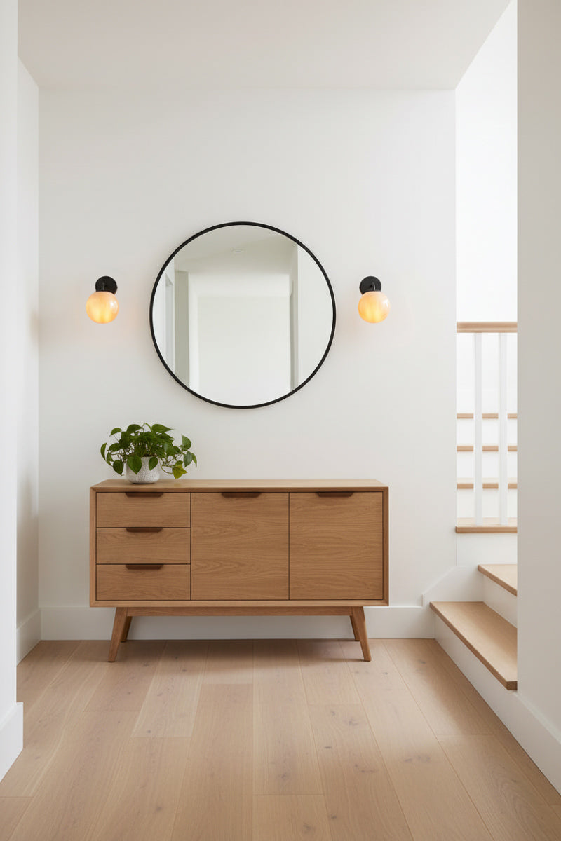 Two abmber glass ball wall sconces with black hardware either side of a round mirror in a natural light-filled stair landing. 