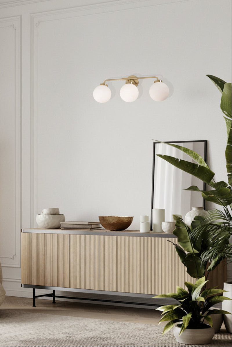 Brass finished triple wall light with opal spherical glass shades above a buffet in a modern living space. 
