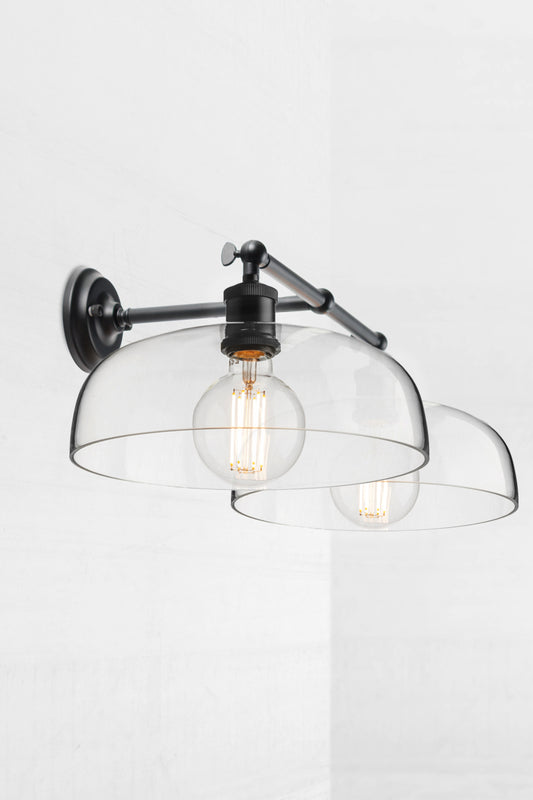 Black double swivel wall light, showing the knuckle joint, with two smooth clear glass shades. 