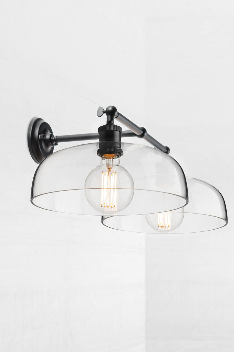 Black double swivel wall light, showing the knuckle joint, with two smooth clear glass shades. 