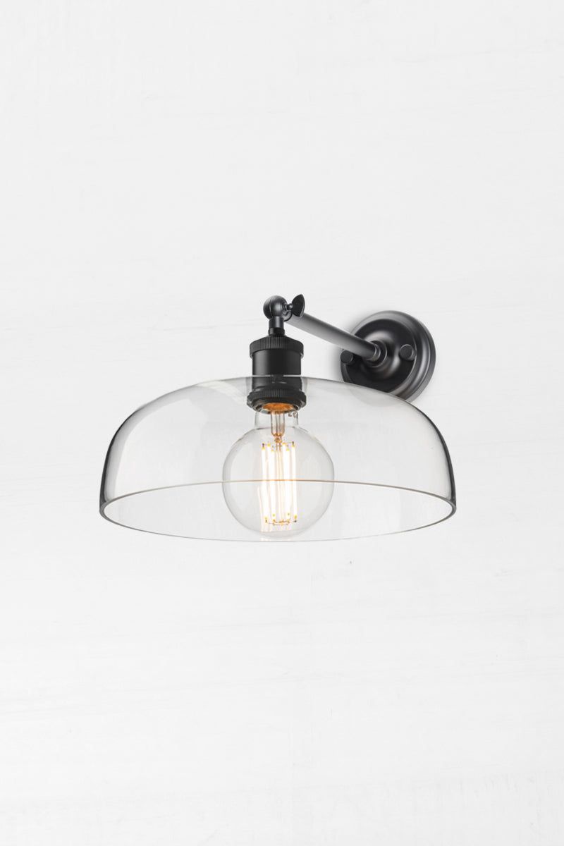 Black straight long arm wall sconce with a large clear glass shade and round bulb. 
