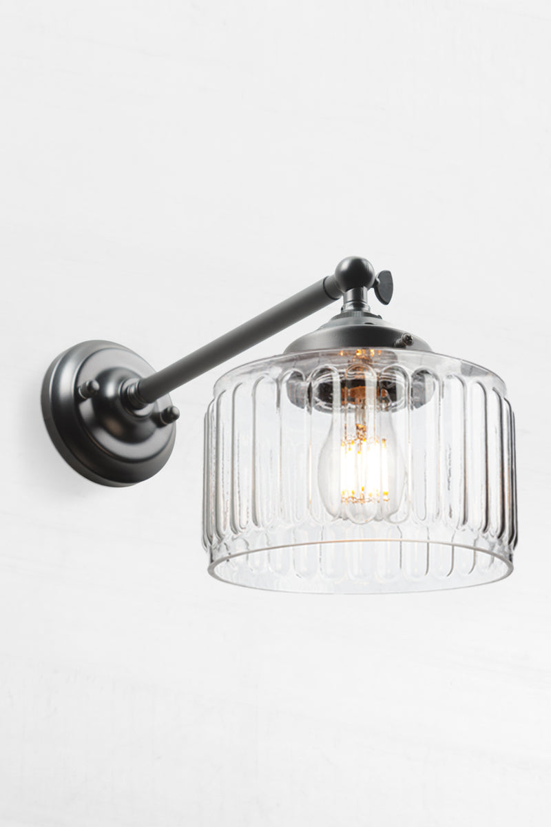 Clear glass shade with vintage fluted detailing on a long straight arm wall sconce with a swivel lampholder. 