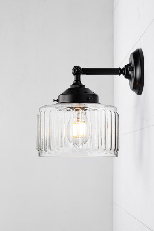 Clear glass shade with vintage fluted detailing on a short, black straight arm wall sconce with a swivel lampholder. 