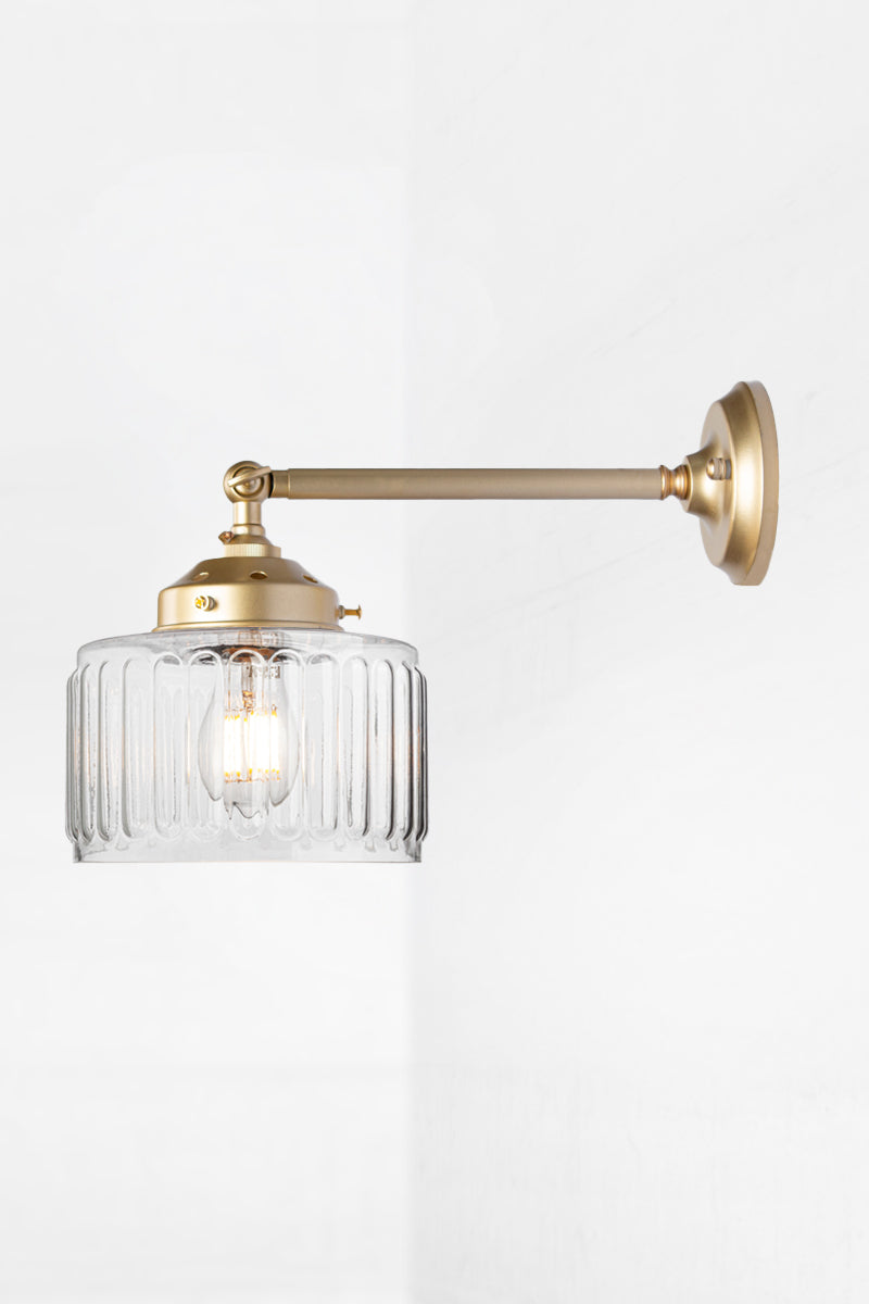 Clear glass shade with vintage fluted detailing on a long, gold/brass straight arm wall sconce with a swivel lampholder. 