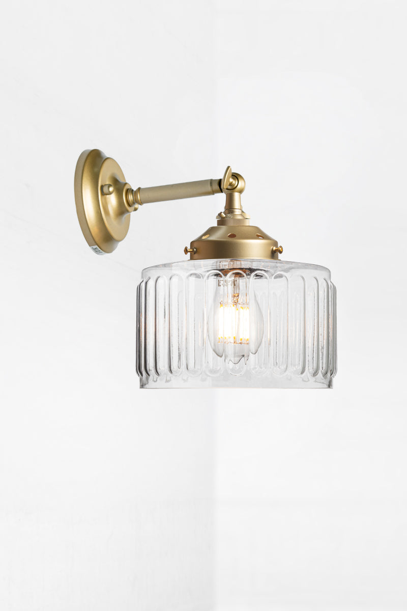 Clear glass shade with vintage fluted detailing on a short, gold/brass straight arm wall sconce with a swivel lampholder. 