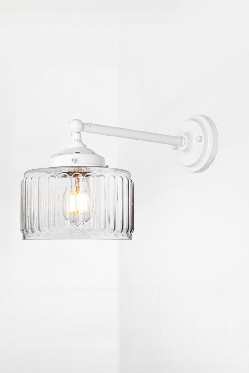 Clear glass shade with vintage fluted detailing on a long, white straight arm wall sconce with a swivel lampholder. 